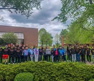 Students wearing Greek letter shirts standing together on an overcast day