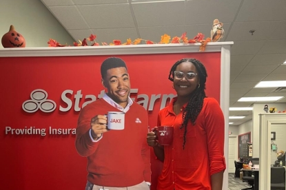 Shalea Byrd at internship with Robin Fowler State Farm enjoys a cup of coffee next to cut out of Jake from State Farm