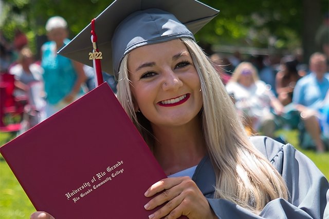 Graduate in grey cap and gown smiling with degree.