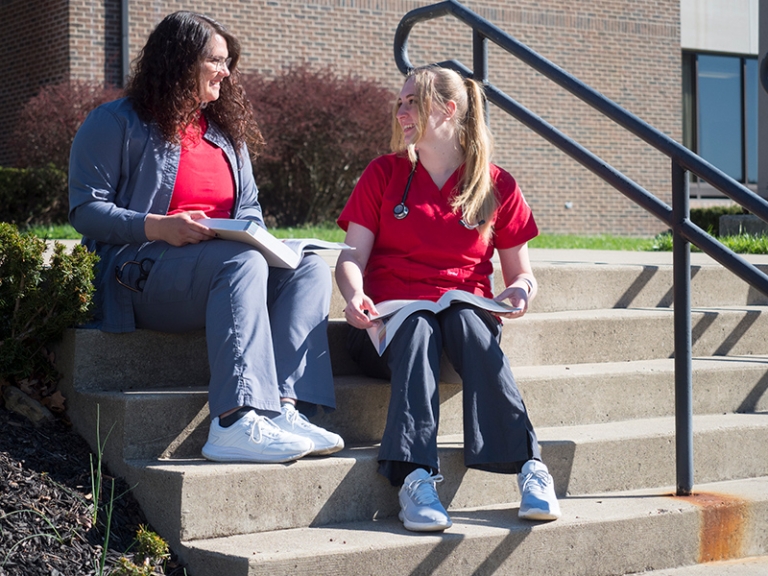 Two nursing students study outside on steps